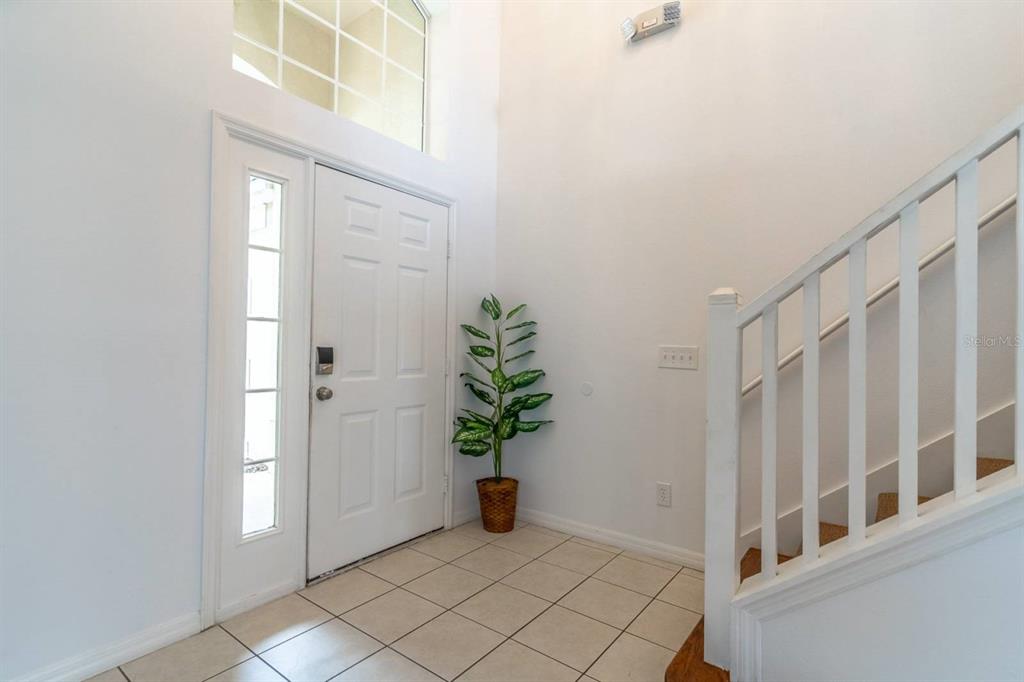 A bright entryway features white walls, tile flooring, a front door, and a wooden staircase — 8512 SUNRISE KEY DRIVE, KISSIMMEE, FL
