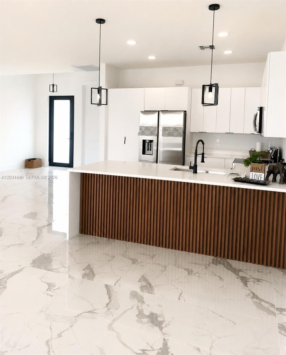 A modern kitchen features white cabinets, a slatted wood island, and marble-patterned tile flooring — 1144 Ecstasy ST E, Lehigh Acres FL 33974, LEHIGH ACRES, FL