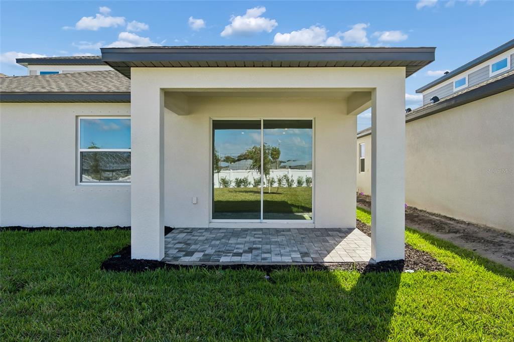 A covered patio with paver flooring sits outside a house with a sliding glass door — 4710 OUTHAUL RUN, PALMETTO, FL