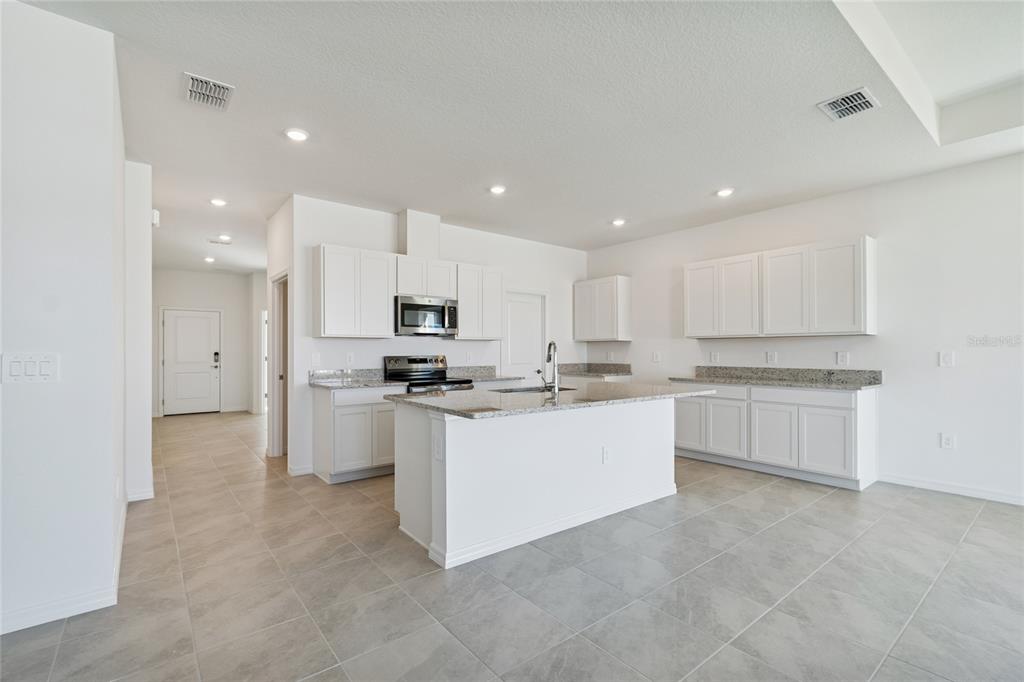 A modern kitchen features white cabinetry, granite countertops, a center island, and light tile flooring — 4710 OUTHAUL RUN, PALMETTO, FL