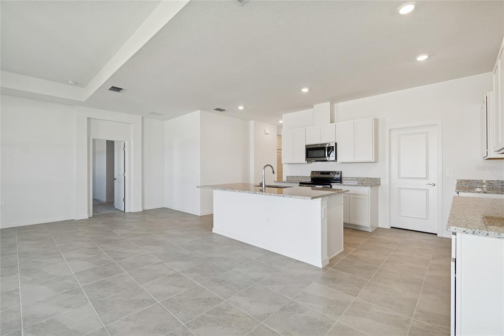 A kitchen with white cabinets, granite countertops, a center island, and light-colored tile flooring — 4710 OUTHAUL RUN, PALMETTO, FL