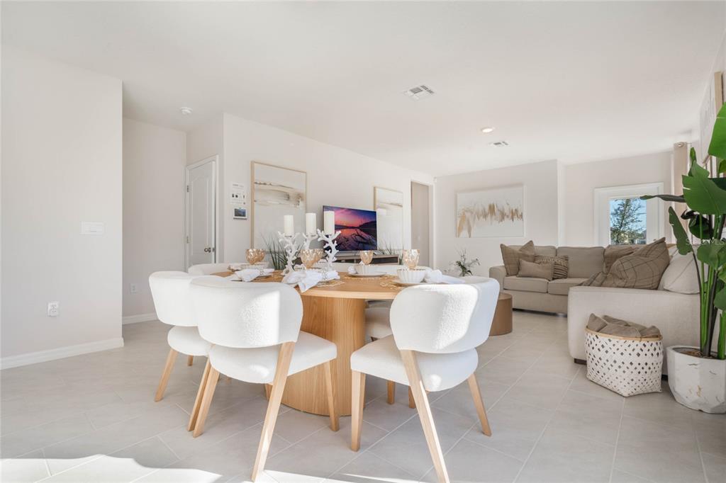 A dining area with a round wooden table and white chairs opens into a living room — 3023 VICEROY, POINCIANA, FL