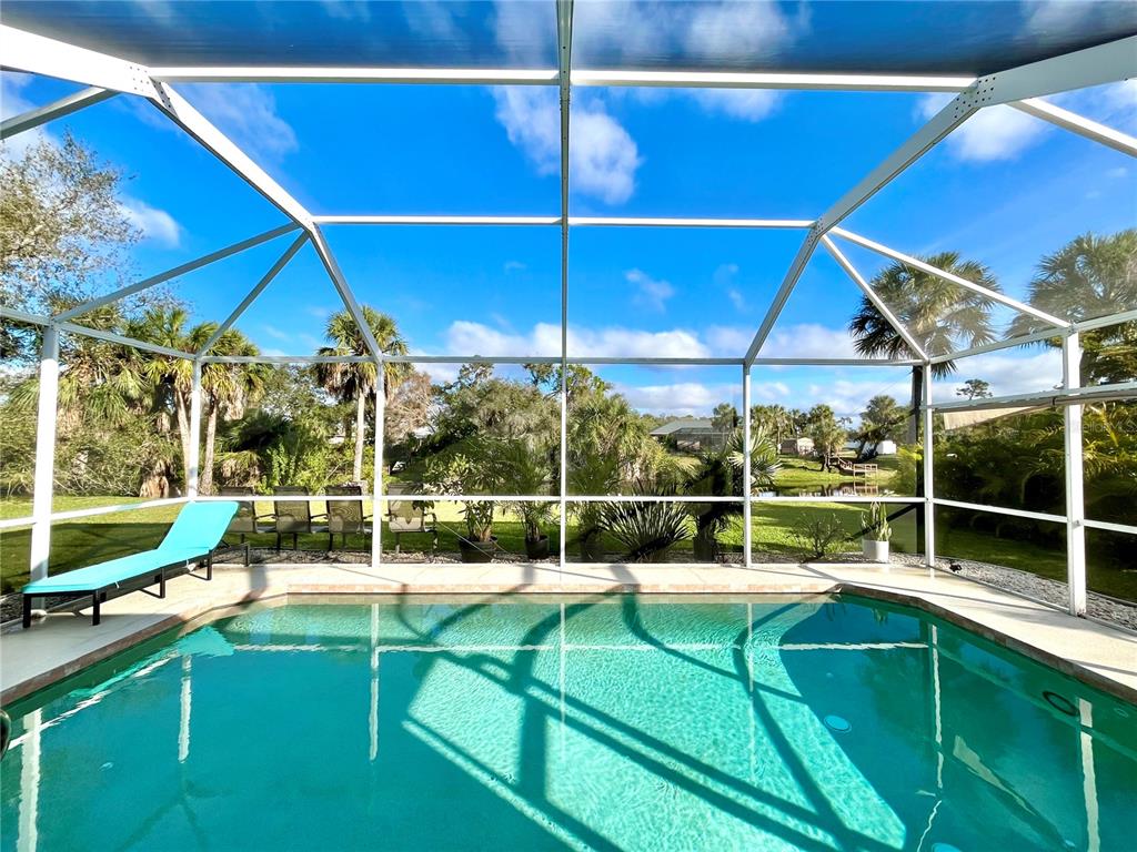 A swimming pool is enclosed by a screened lanai with a view of palm trees — 1268 W HILLSBOROUGH BOULEVARD, NORTH PORT, FL