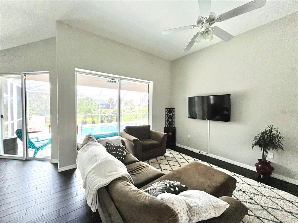 A living room features dark wood floors, a mounted television, and sliding glass doors to a pool — 1268 W HILLSBOROUGH BOULEVARD, NORTH PORT, FL
