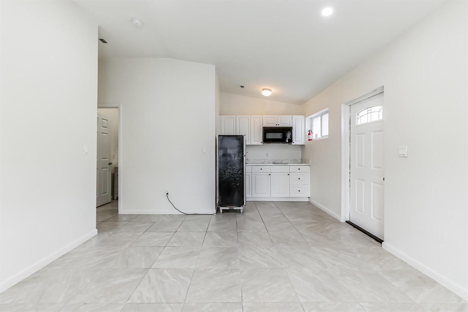 A kitchen area features white cabinets, a black refrigerator, and light-colored tile flooring — 13961 SW 156th Terrace, Miami FL 33177, MIAMI, FL
