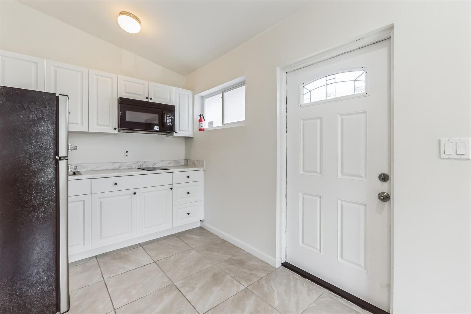A small kitchen features white cabinets, a black microwave, a dark refrigerator, and tile flooring — 13961 SW 156th Terrace, Miami FL 33177, MIAMI, FL