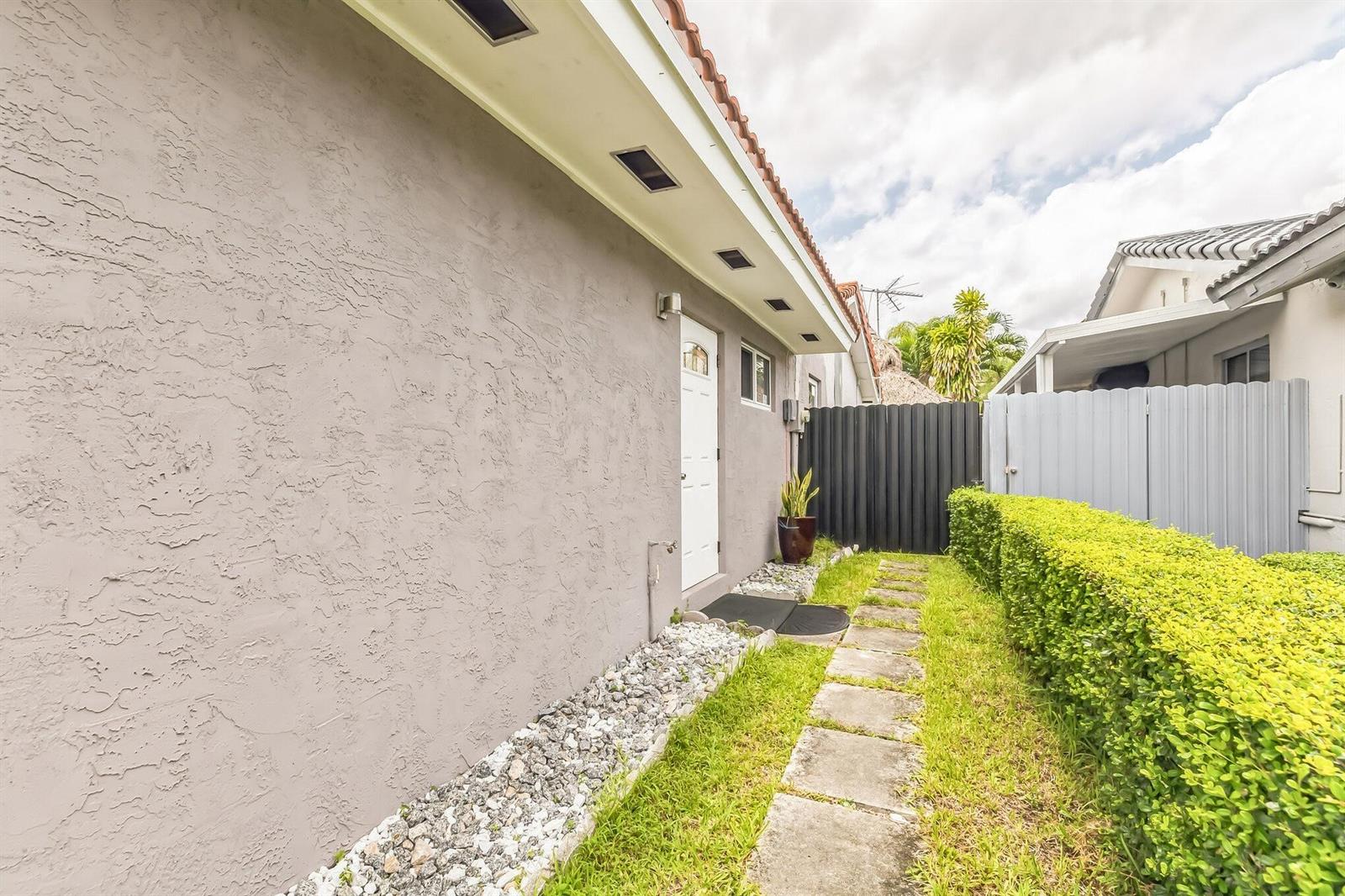 A side exterior view of a house with a stucco wall, walkway, and hedge — 13961 SW 156th Terrace, Miami FL 33177, MIAMI, FL