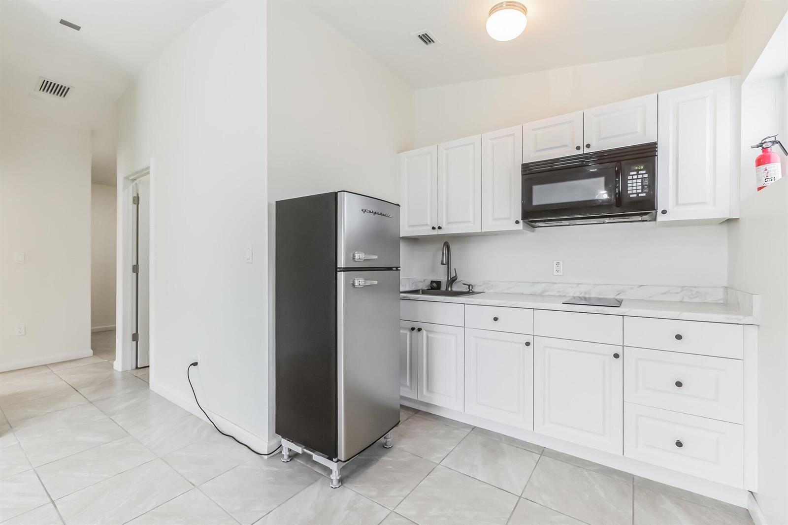 A small kitchen features white cabinets, a stainless steel refrigerator, and a black microwave — 13961 SW 156th Terrace, Miami FL 33177, MIAMI, FL