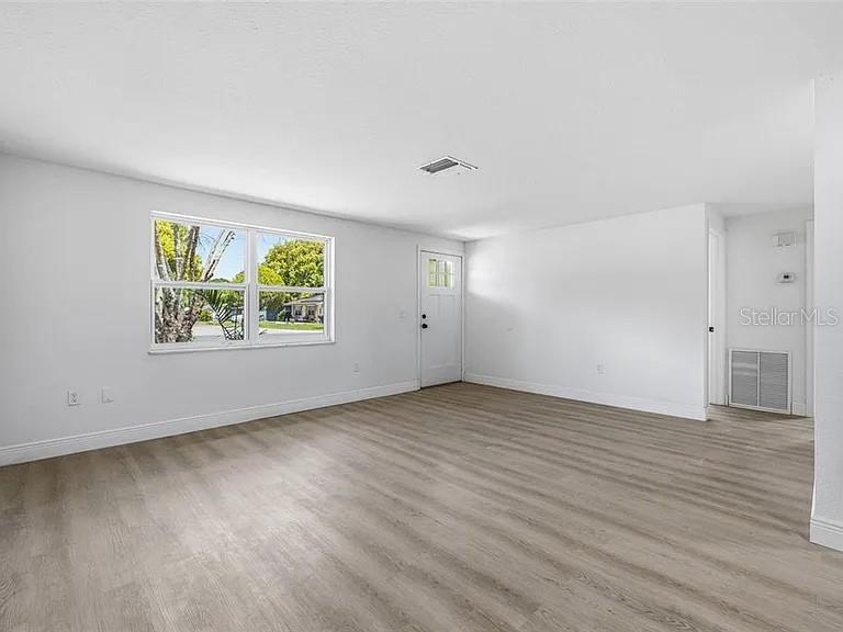 An empty living room features white walls, light wood-look flooring, and a white entry door — 39252 HEIGHTS AVENUE, ZEPHYRHILLS, FL