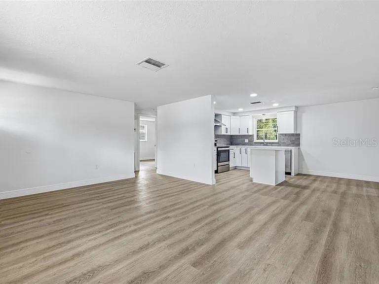 An open-concept living area features light wood-look flooring and a kitchen with white cabinetry — 39252 HEIGHTS AVENUE, ZEPHYRHILLS, FL