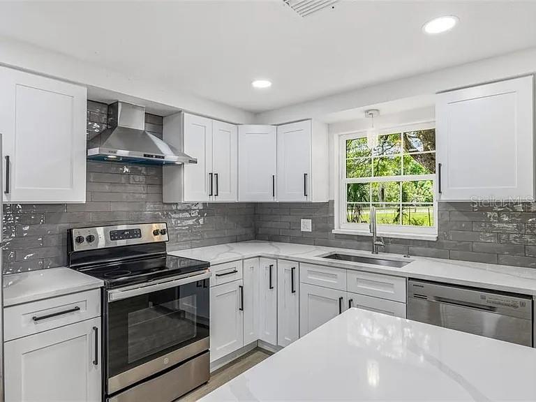 A modern kitchen features white cabinets, gray subway tile backsplash, and stainless steel appliances — 39252 HEIGHTS AVENUE, ZEPHYRHILLS, FL