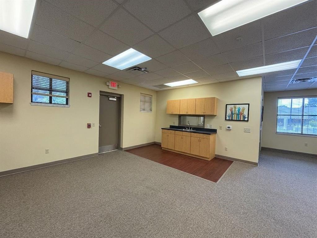 An office or classroom space with beige walls, carpeted flooring, a kitchenette, and two windows — 578 OCOEE COMMERCE PARKWAY, OCOEE, FL