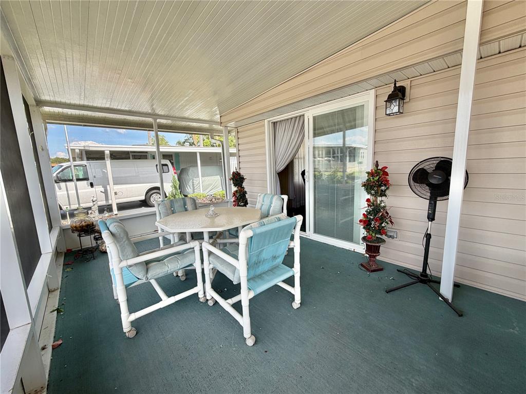 A covered patio features a white table with four chairs, a standing fan, and siding — 100 MARIGOLD STREET, LEESBURG, FL