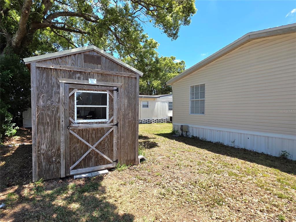 A wooden shed stands next to a beige mobile home on a grassy lot — 37251 LOIS AVENUE, ZEPHYRHILLS, FL