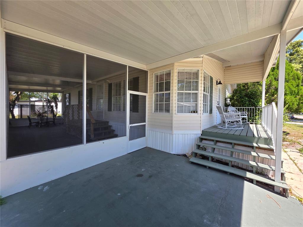 A covered patio with a screened-in area and wooden steps leading to a house entrance — 37251 LOIS AVENUE, ZEPHYRHILLS, FL