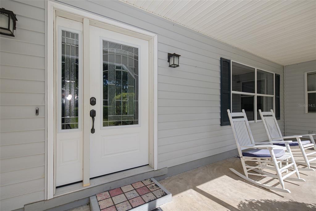 A white front door with a sidelight and two rocking chairs on a covered porch — 39 WOOD RIDGE DRIVE, OCALA, FL
