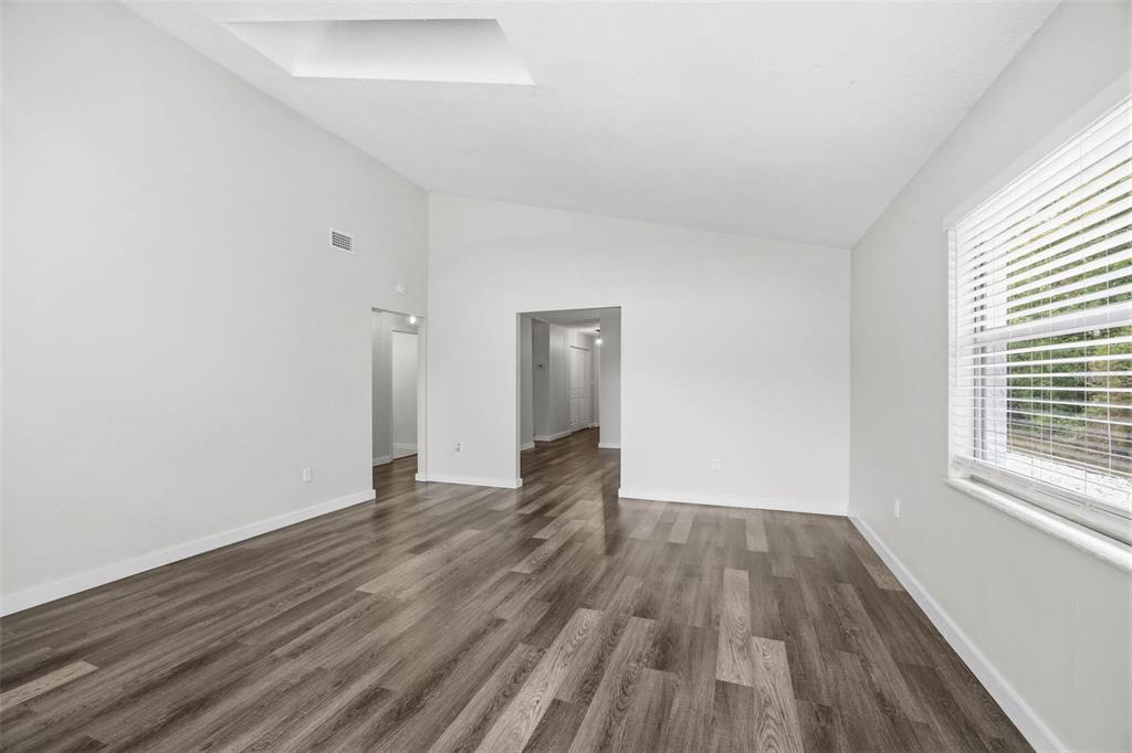 An empty living room features light gray walls, wood-look flooring, and a vaulted ceiling — 2801 51ST AVENUE S, ST PETERSBURG, FL
