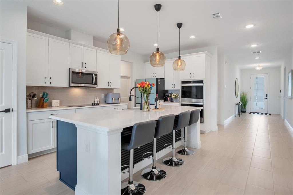 A modern kitchen features a blue island with bar stools, white cabinetry, and pendant lighting — 18863 RAWSON STREET, ORLANDO, FL