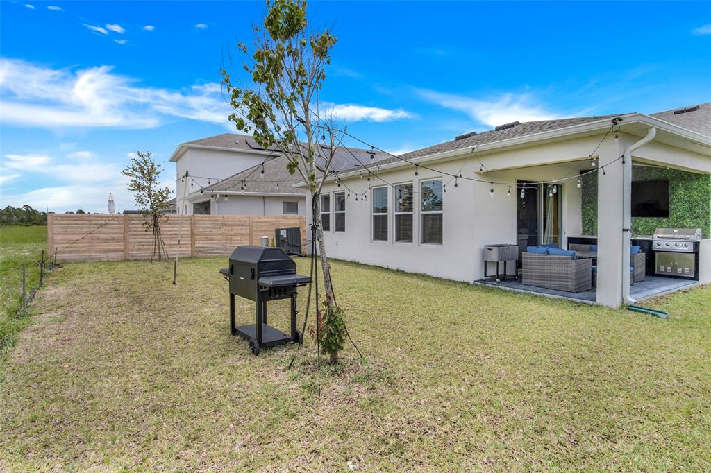 A backyard features a patio with a grill, string lights, and a wooden privacy fence — 18863 RAWSON STREET, ORLANDO, FL
