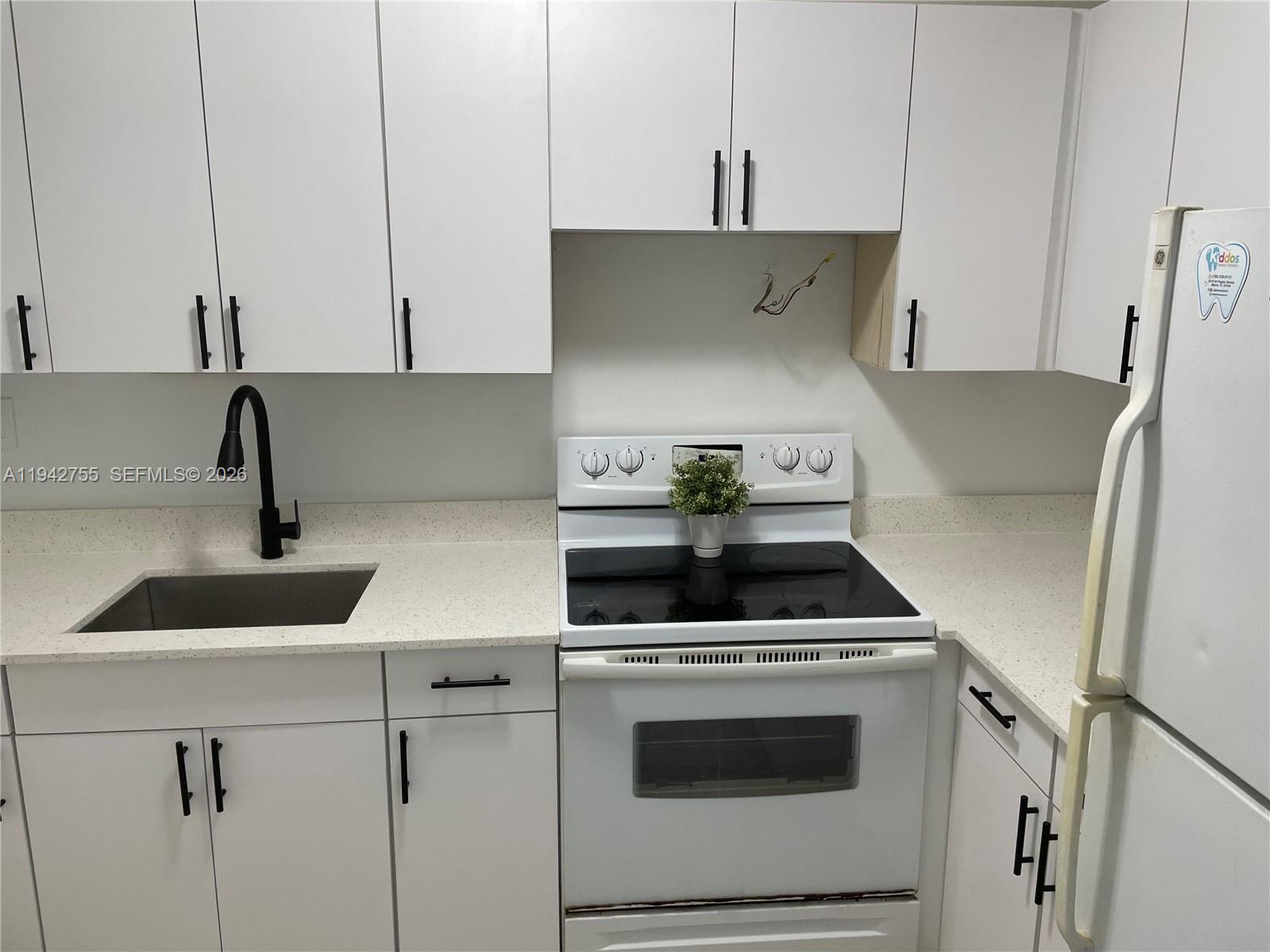 A kitchen features white cabinets, a black faucet, a white stove, and light-colored countertops — 142 SW 18th Ave # 19, Miami FL 33135, MIAMI, FL