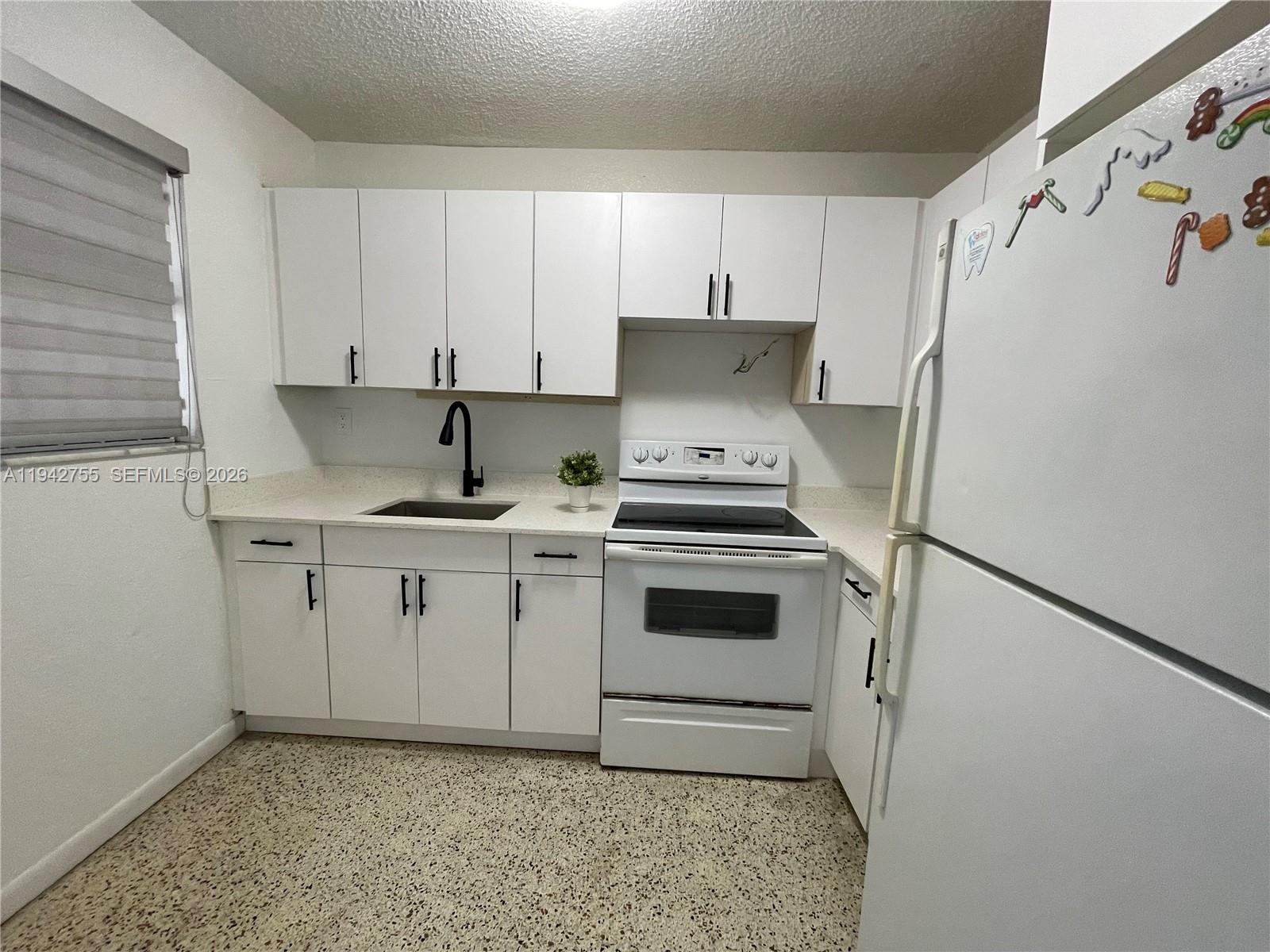 A small kitchen features white cabinets, a white stove, a sink, and speckled flooring — 142 SW 18th Ave # 19, Miami FL 33135, MIAMI, FL