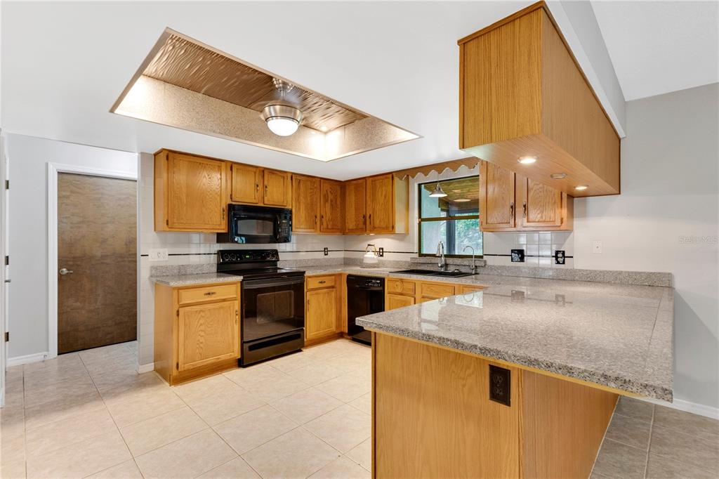 A kitchen features oak cabinets, granite countertops, black appliances, and a recessed ceiling light fixture — 3292 MAJESTIC OAK DRIVE, ST CLOUD, FL