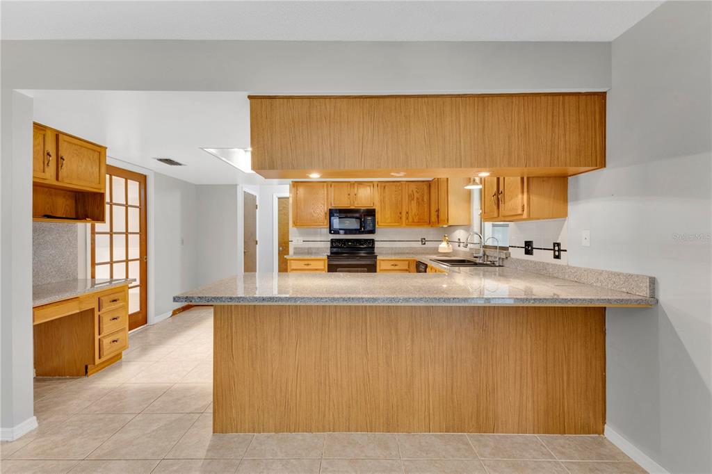 A kitchen features oak cabinets, granite countertops, a breakfast bar, and light-colored tile flooring — 3292 MAJESTIC OAK DRIVE, ST CLOUD, FL