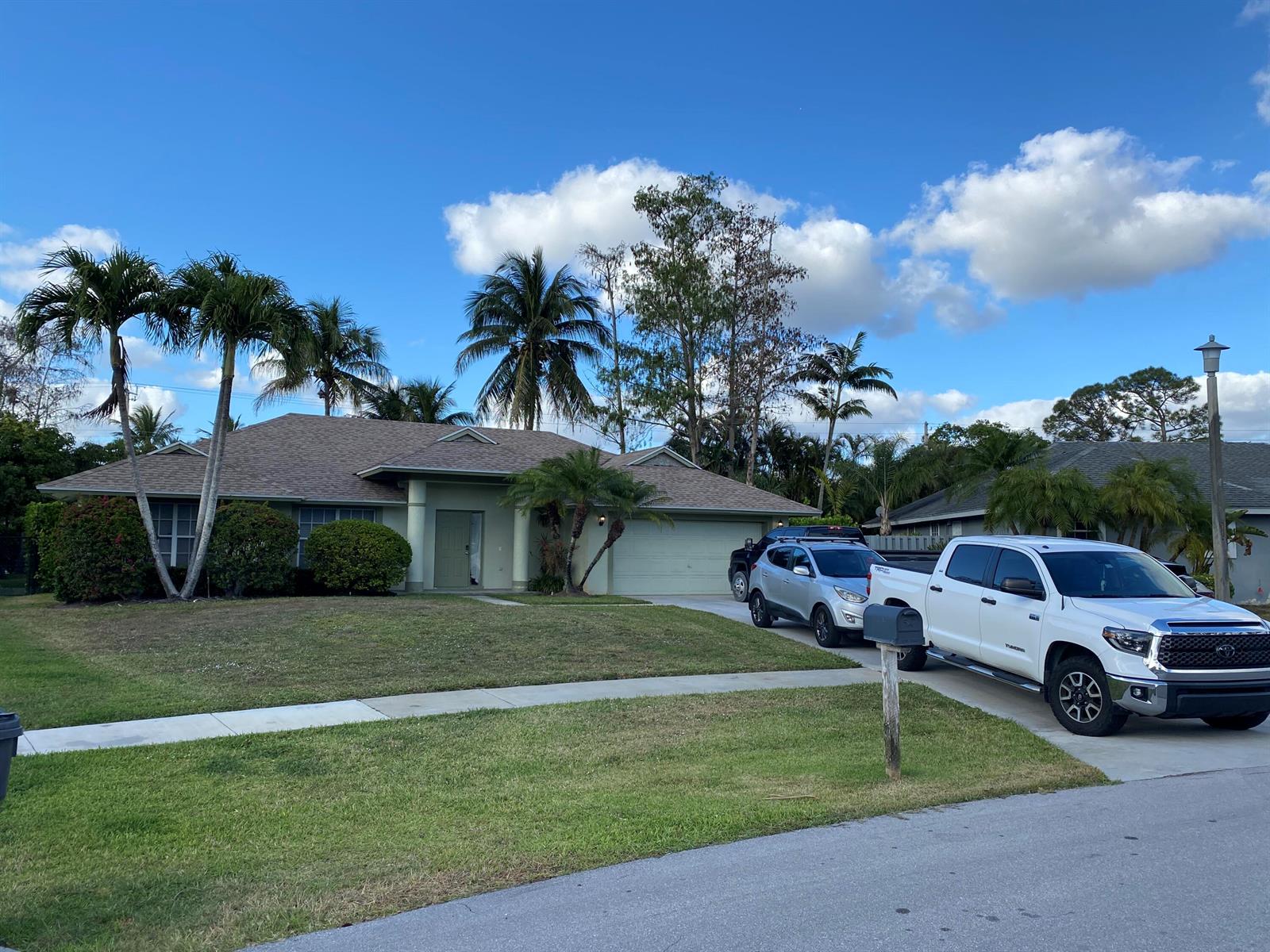 A single-story house with a light-colored exterior, palm trees, and two vehicles in the driveway — 1094 Raintree Lane, Wellington FL 33414, WELLINGTON, FL