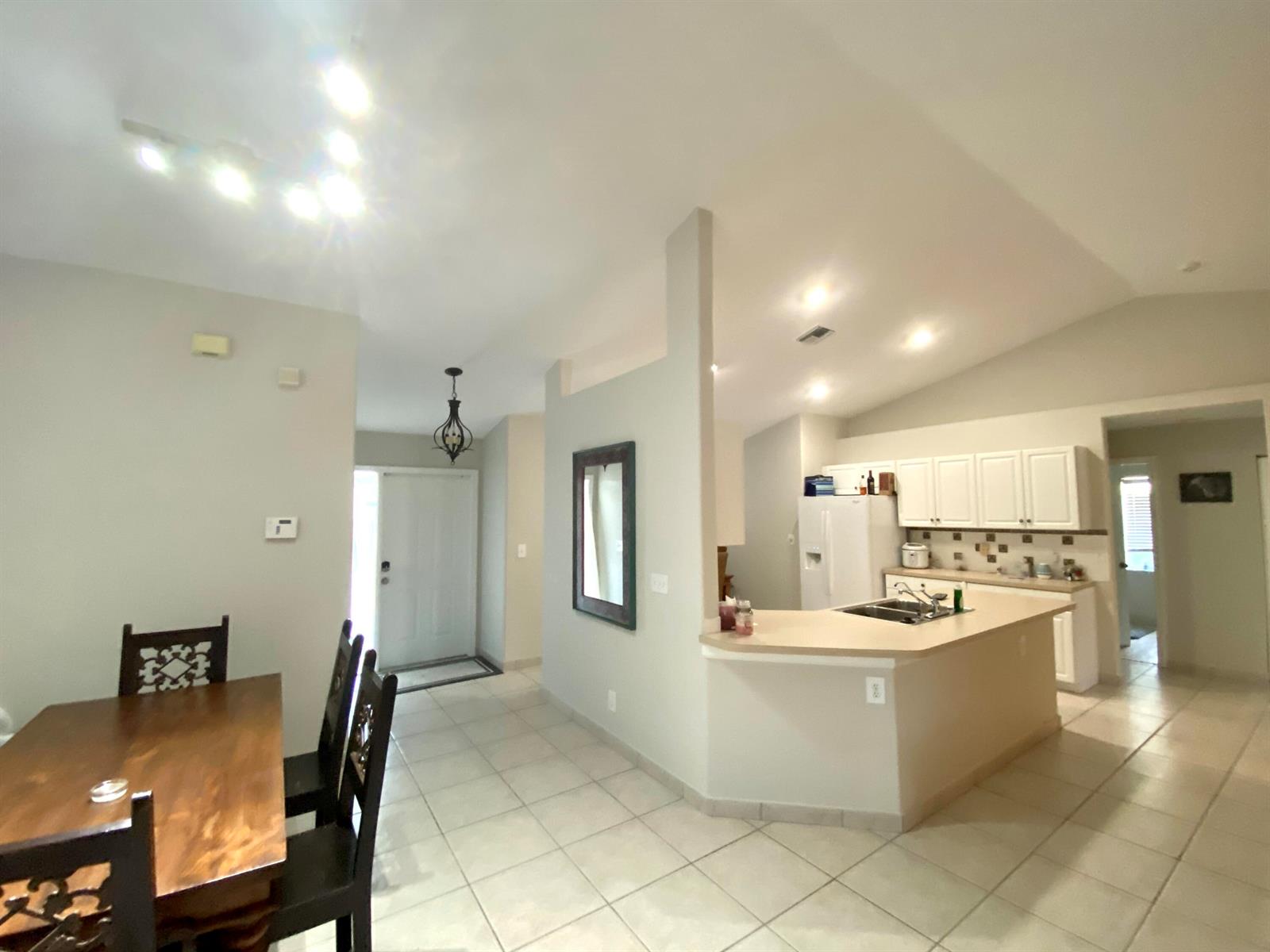 A dining area with a wooden table leads to an open kitchen with white cabinets — 1094 Raintree Lane, Wellington FL 33414, WELLINGTON, FL