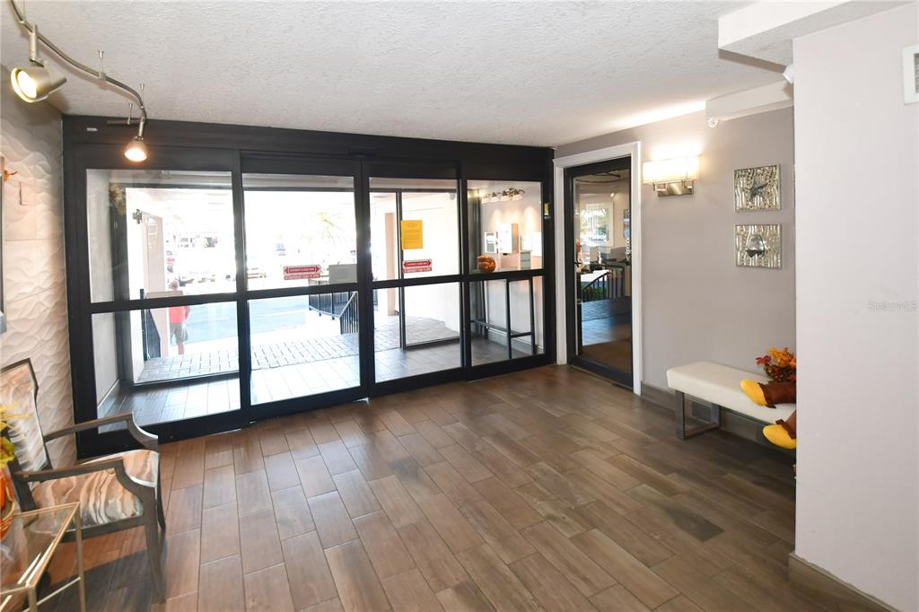 A lobby area features wood-look tile flooring, glass sliding doors, and a small bench — 51 ISLAND WAY UNIT 909, CLEARWATER, FL