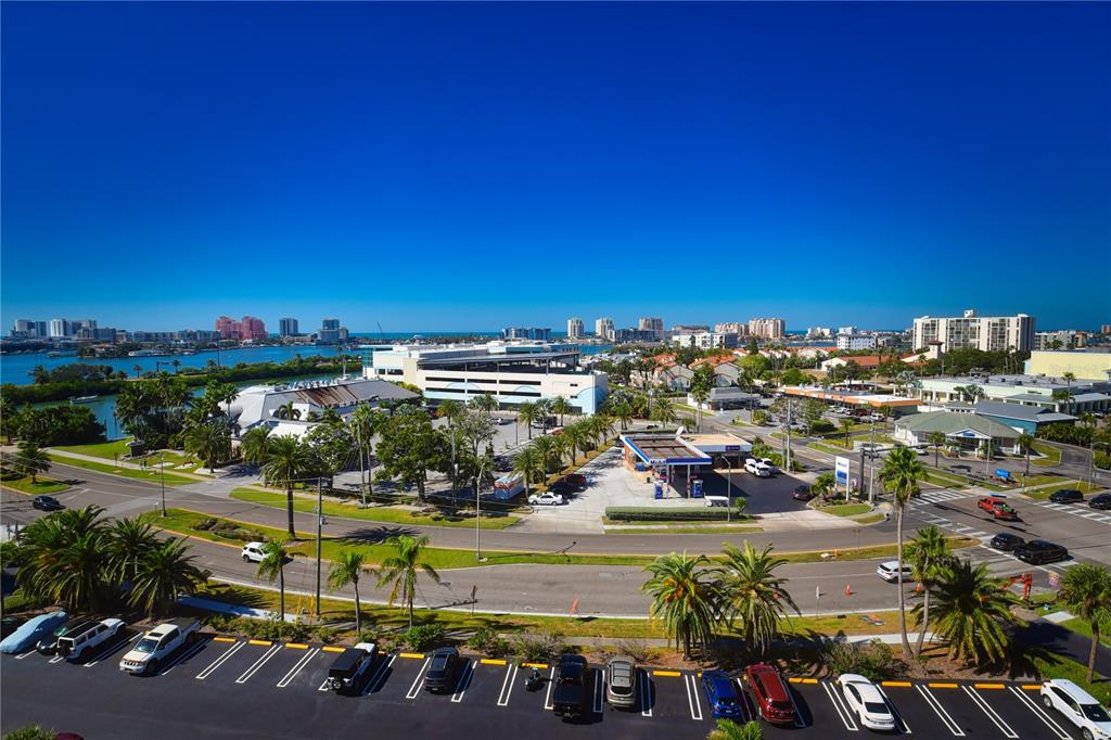 An elevated view shows a parking lot, a gas station, and coastal buildings under clear skies — 51 ISLAND WAY UNIT 909, CLEARWATER, FL