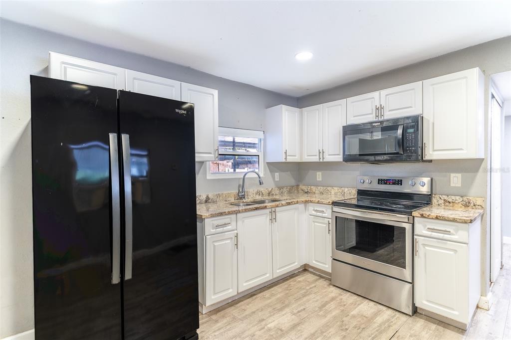 A kitchen features white cabinets, granite countertops, stainless steel appliances, and a black refrigerator — 5807 BARRY LANE, TAMPA, FL