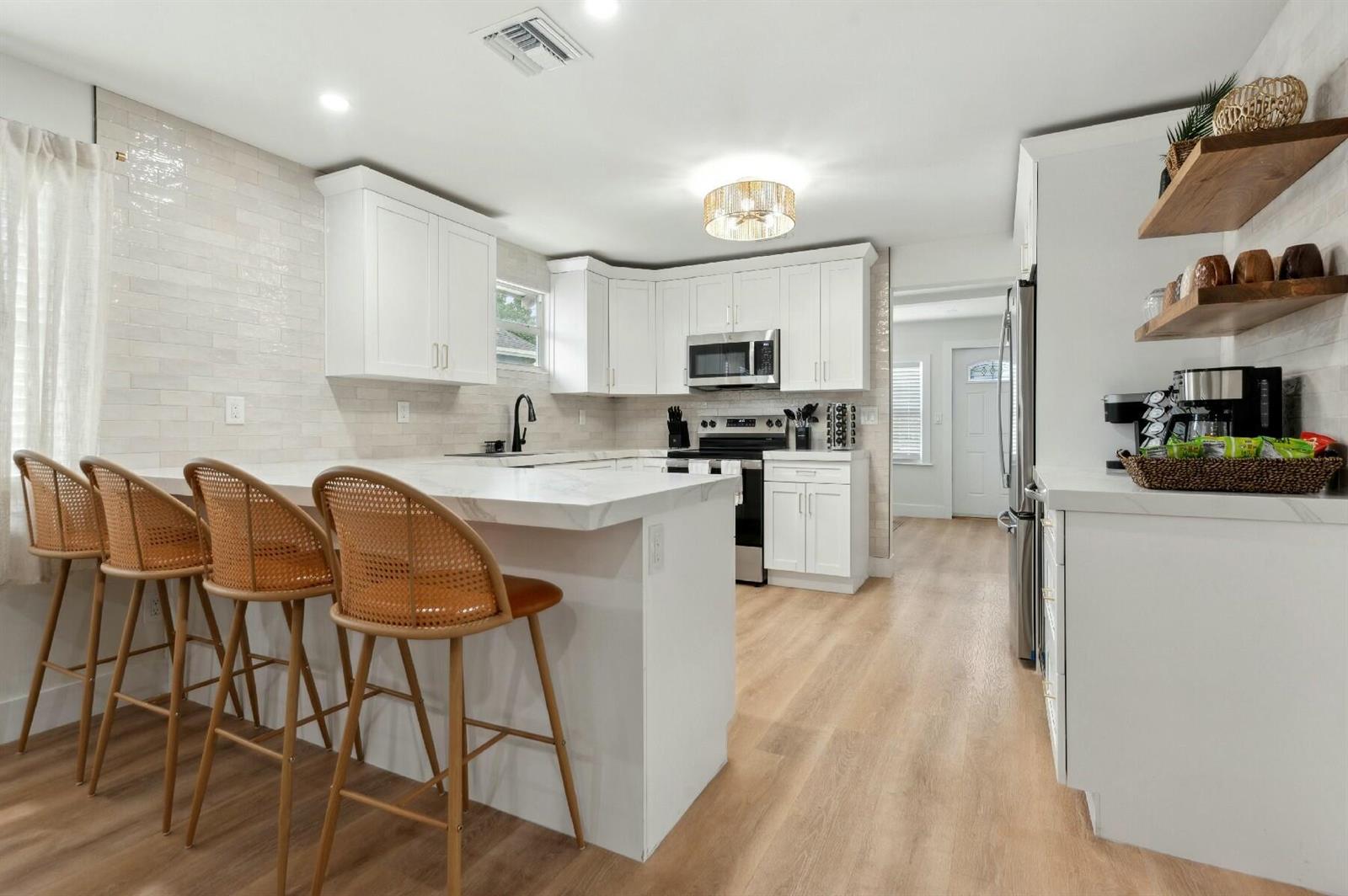 A modern kitchen features white cabinetry, marble-look countertops, a breakfast bar, and light wood flooring — 125 NW 3rd Avenue, Delray Beach FL 33444, DELRAY BEACH, FL