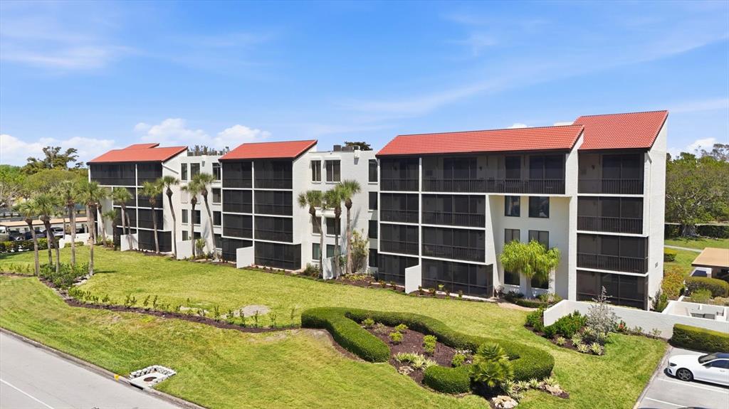 An exterior view of a multi-story apartment building with red tile roofs and screened balconies — 1955 GULF OF MEXICO DR UNIT G6-311, LONGBOAT KEY, FL