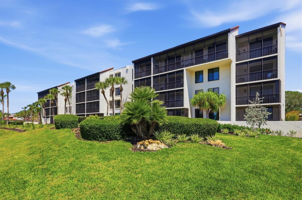 A multi-story apartment building with screened balconies sits behind a landscaped lawn and palm trees — 1955 GULF OF MEXICO DR UNIT G6-311, LONGBOAT KEY, FL
