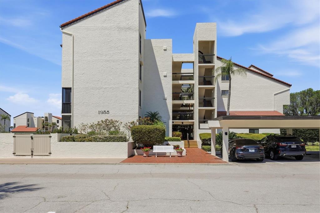 A multi-story apartment building features a white stucco exterior, open-air walkways, and a covered carport — 1955 GULF OF MEXICO DR UNIT G6-311, LONGBOAT KEY, FL