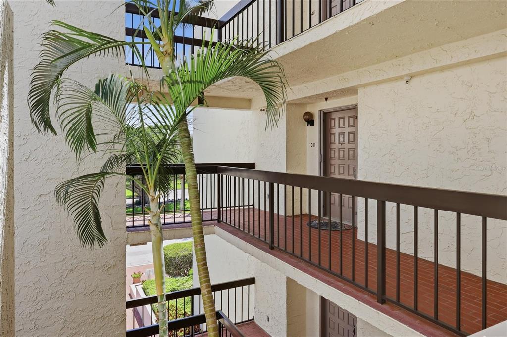 An exterior view of a multi-story apartment building with open-air walkways and a palm tree — 1955 GULF OF MEXICO DR UNIT G6-311, LONGBOAT KEY, FL