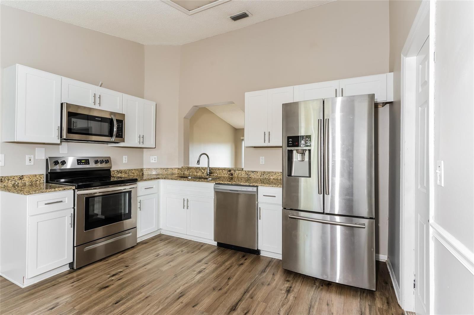 A kitchen features white cabinets, stainless steel appliances, granite countertops, and wood-look flooring — 1890 4th Avenue, Vero Beach FL 32962, VERO BEACH, FL