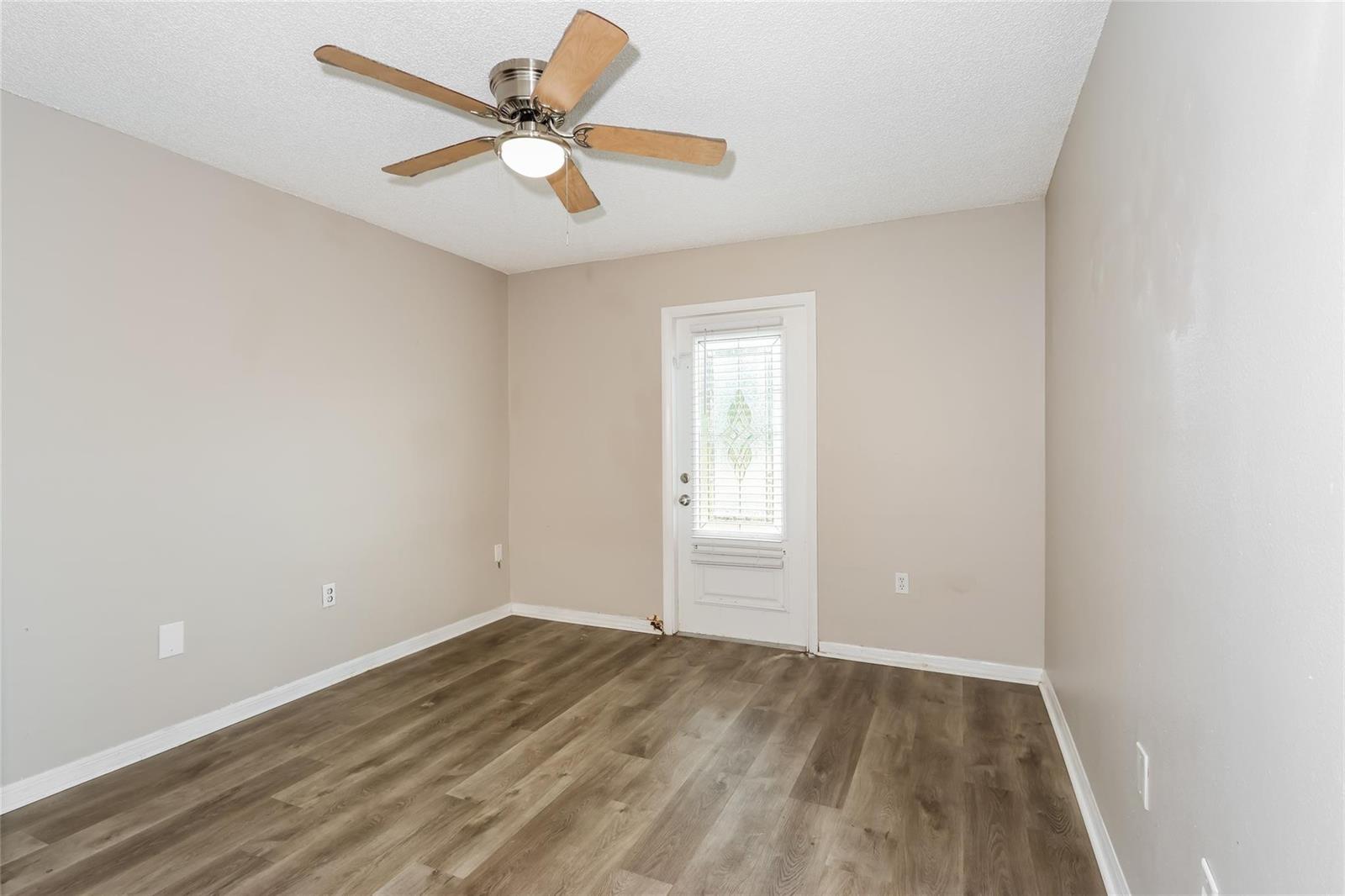 An empty room features light-colored walls, wood-look flooring, a ceiling fan, and a glass-paneled door — 1890 4th Avenue, Vero Beach FL 32962, VERO BEACH, FL