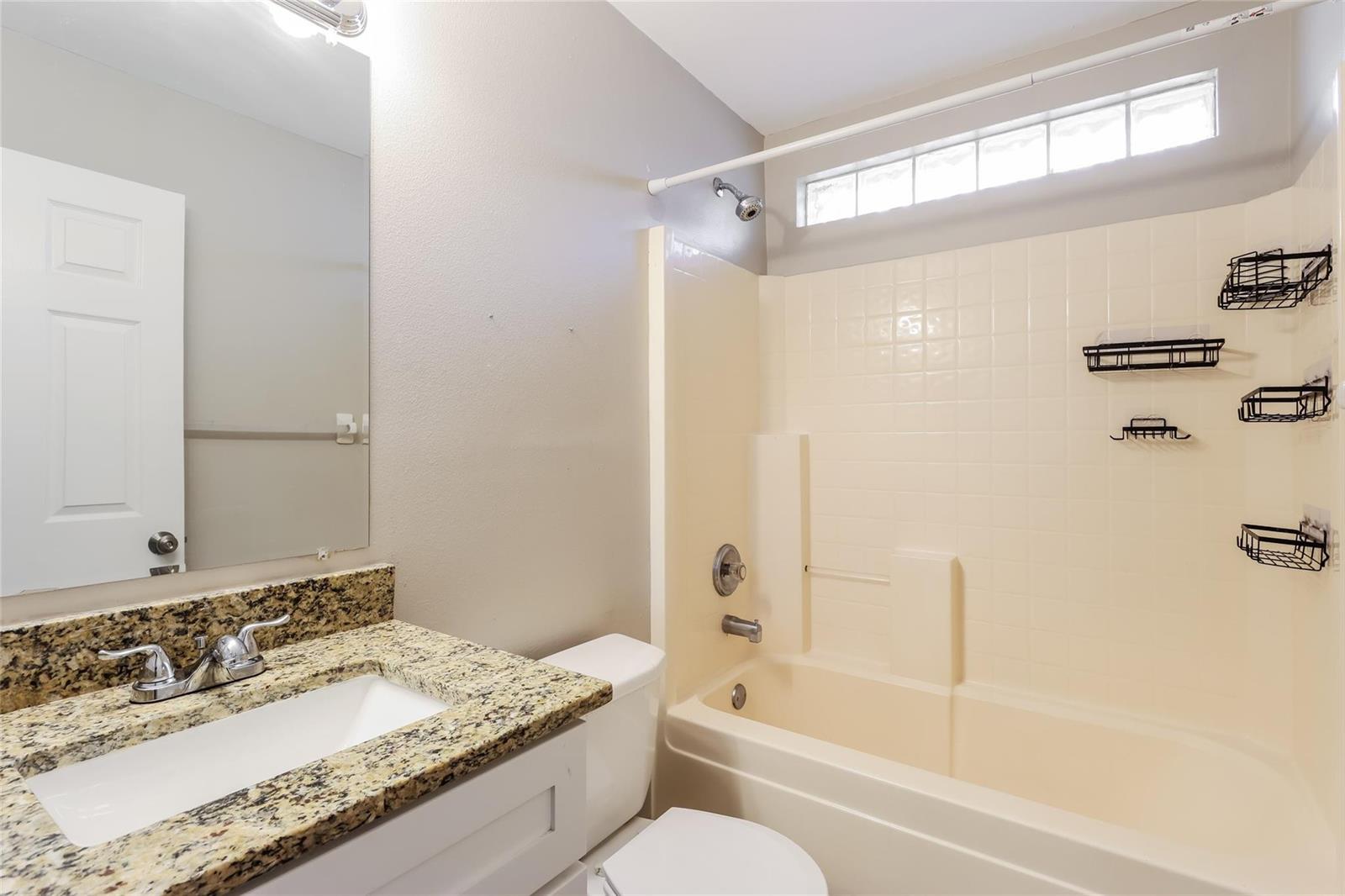 A bathroom features a granite vanity, a white sink, a toilet, and a tiled tub-shower — 1890 4th Avenue, Vero Beach FL 32962, VERO BEACH, FL