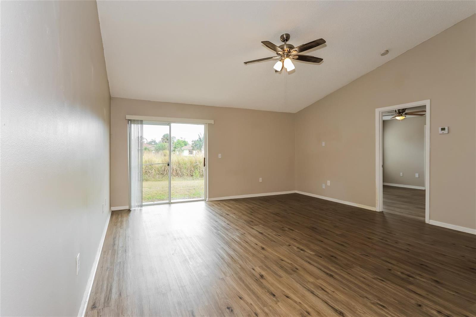 An empty living room with wood-look flooring, a ceiling fan, and a sliding glass door — 1890 4th Avenue, Vero Beach FL 32962, VERO BEACH, FL