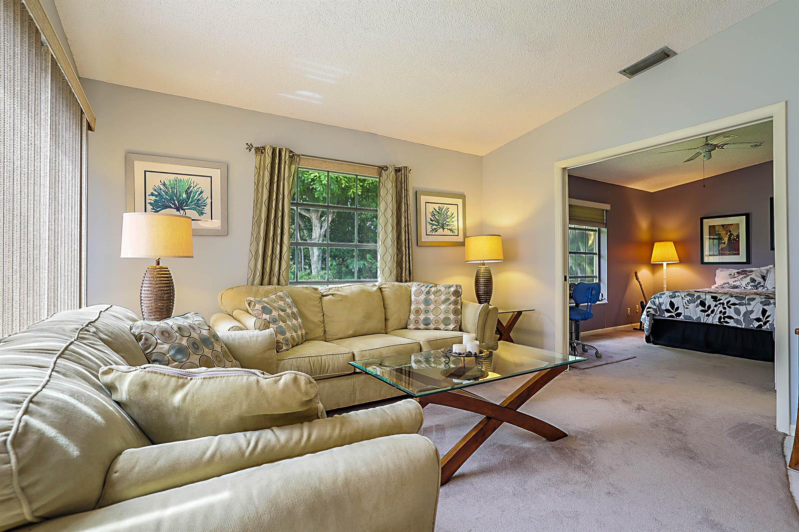 A living room with a beige sofa and glass coffee table opens into a bedroom — 5231 Copperleaf Circle, Delray Beach FL 33484, DELRAY BEACH, FL