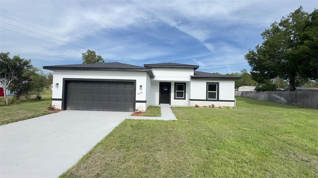 A single-story house with a white stucco exterior, black trim, and a two-car garage — 9848 N CORTLANDT DRIVE, CITRUS SPRINGS, FL