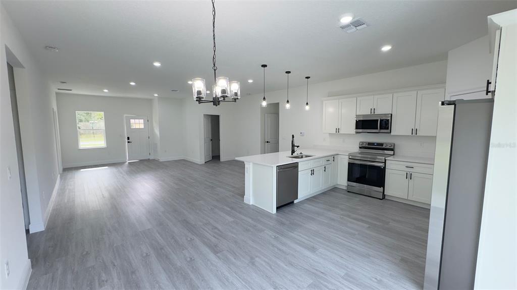 An open-concept kitchen and living area features white cabinetry, stainless steel appliances, and gray flooring — 9848 N CORTLANDT DRIVE, CITRUS SPRINGS, FL