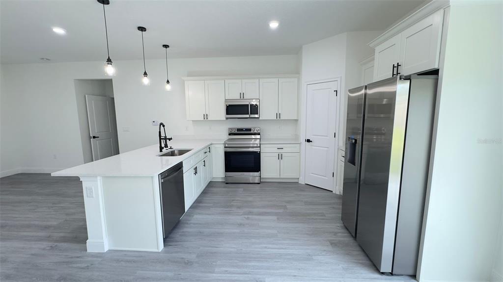 A modern kitchen features white cabinetry, stainless steel appliances, a center island, and gray flooring — 9848 N CORTLANDT DRIVE, CITRUS SPRINGS, FL