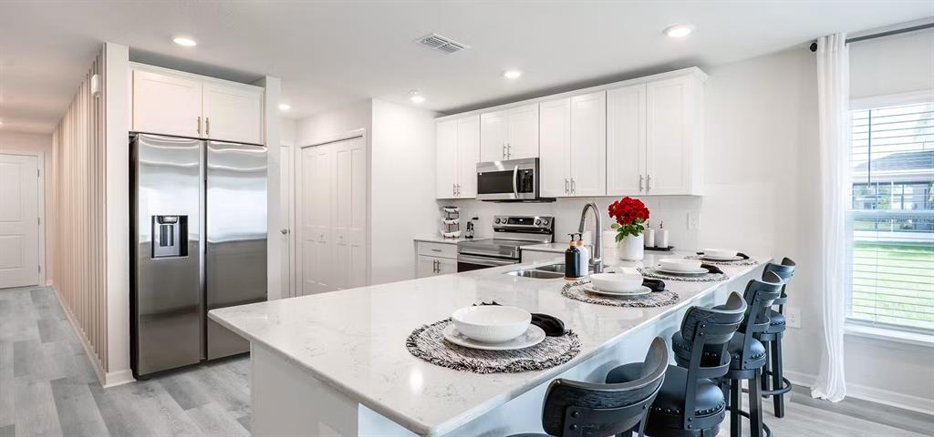 A modern kitchen features white cabinetry, stainless steel appliances, and a large quartz-topped island — 402 CHESAPEAKE DRIVE, ST CLOUD, FL