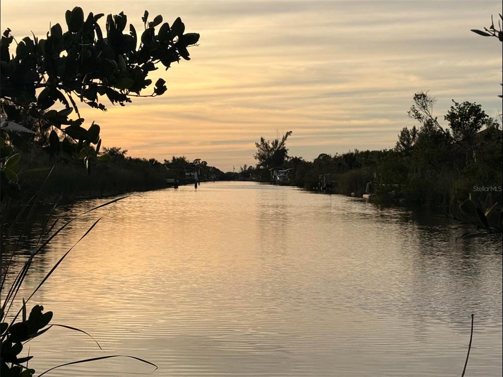 A view of a calm canal at sunset framed by trees and vegetation — 10273 ST PAUL DRIVE, PORT CHARLOTTE, FL