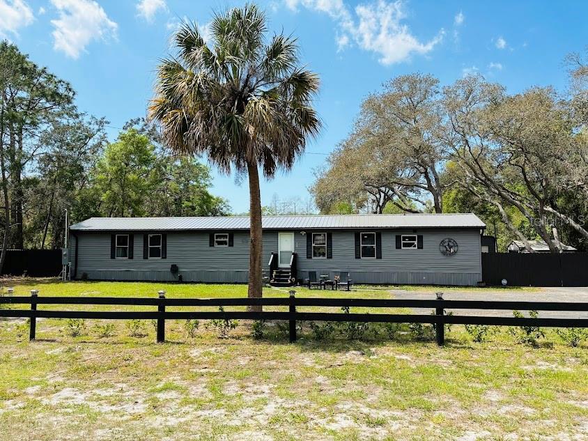 A gray manufactured home with a metal roof sits behind a black wooden fence — 7161 SCHERING STREET, WEEKI WACHEE, FL