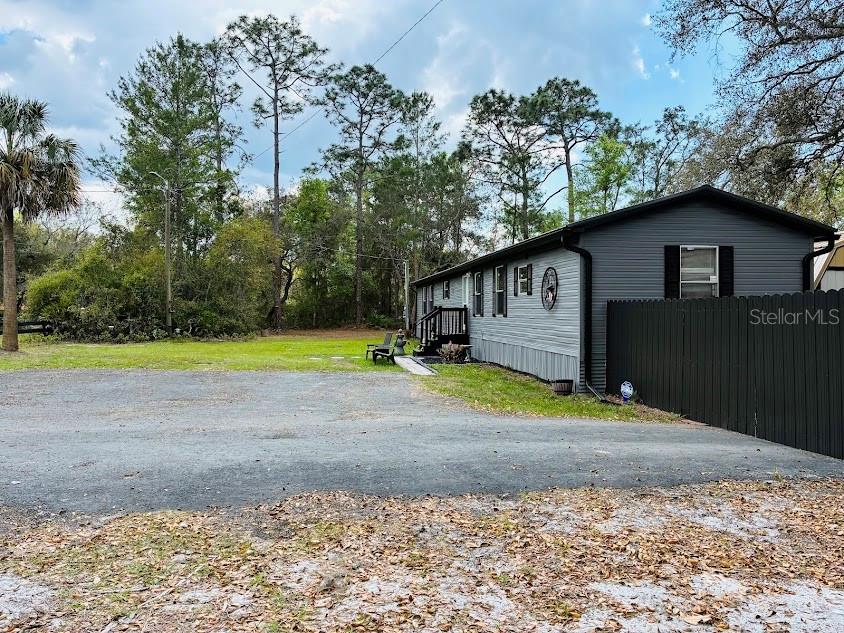 A gray manufactured home sits beside a black privacy fence on a gravel lot — 7161 SCHERING STREET, WEEKI WACHEE, FL