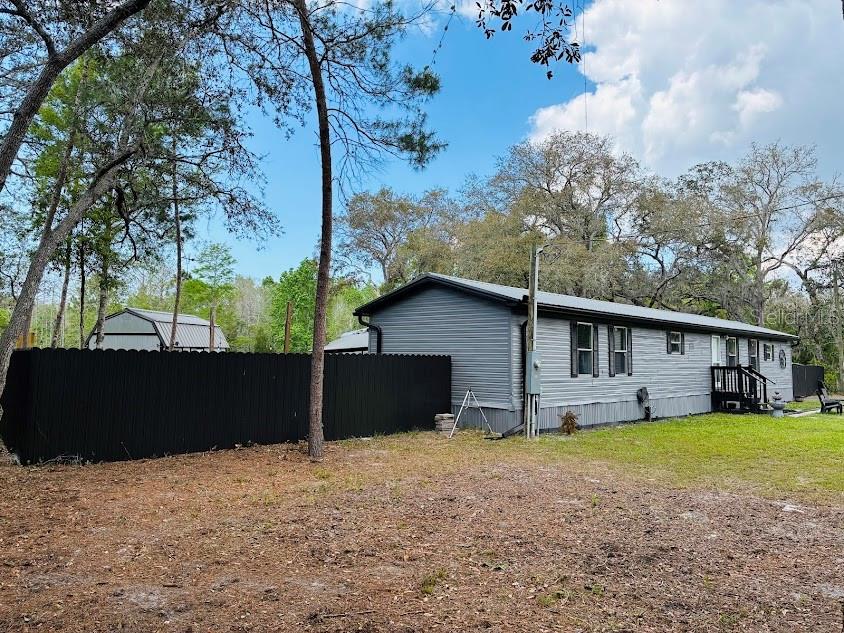 A grey manufactured home sits behind a black privacy fence on a wooded lot — 7161 SCHERING STREET, WEEKI WACHEE, FL